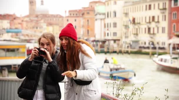 Twee jonge vrouwen nemen foto's van de omgeving in de straten van Venetië - Video