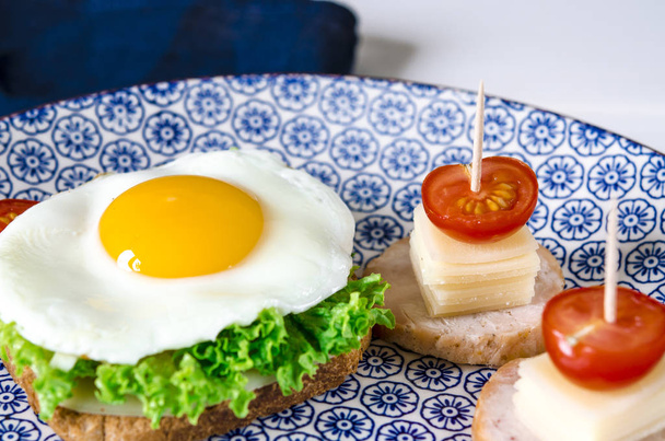 Sandwich con huevo, jamón, queso, tostadas y hojas de ensalada se encuentra en un plato con tomate y eneldo
 - Foto, Imagen