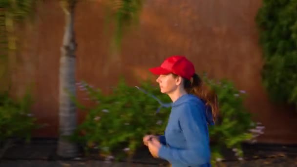 Kobieta biegnie w dół ulicy wśród tropikalnej alei. Zdrowy, aktywny styl życia - Materiał filmowy, wideo