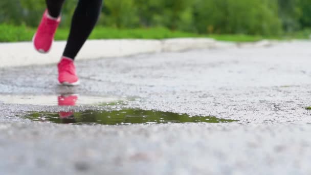 Legs of a runner in sneakers. Sports woman jogging outdoors, stepping into muddy puddle. Single runner running in rain, making splash. Slow motion - Footage, Video