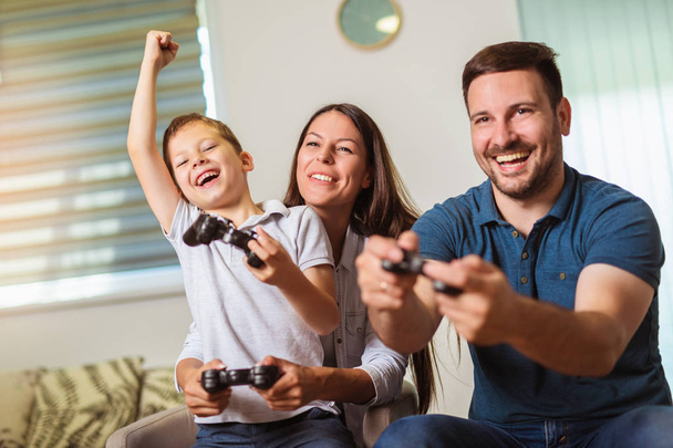 Familia sonriente sentada en el sofá jugando videojuegos
 - Foto, Imagen