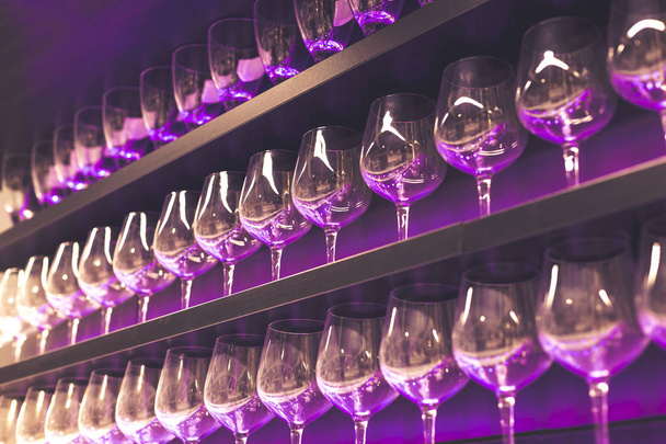 Plank met veel lege wijn glazen met roze en violet licht. Bar of glaswerk winkel interieur. Viering, evenement of feest concept. - Foto, afbeelding