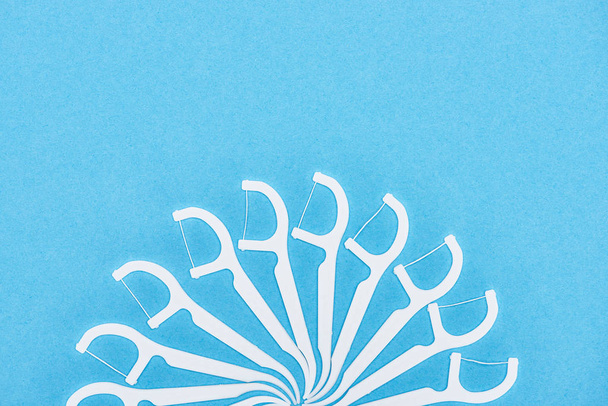 Κορυφαία όψη των λευκών και πλαστικών οδοντογλυφίδων με νήμα που απομονώνονται σε μπλε  - Φωτογραφία, εικόνα