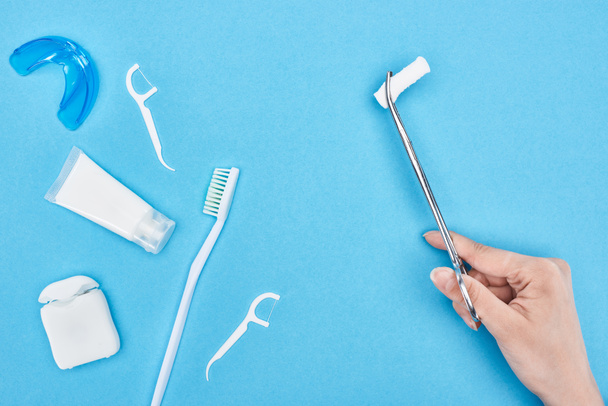 cropped view of woman holding tweezers with cotton pad near toothpaste and toothbrush on blue  - Photo, Image