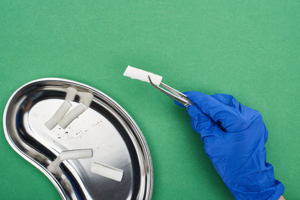 cropped view of dentist holding tweezers with cotton pad near metallic plate on green  - Photo, Image