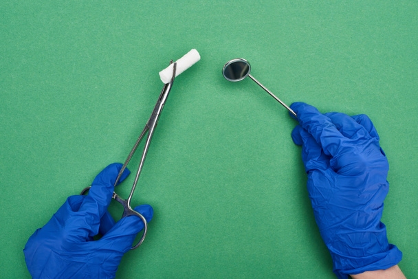 vue recadrée du dentiste en gants de latex bleu tenant des ciseaux avec tampon de coton et miroir médical sur vert
  - Photo, image