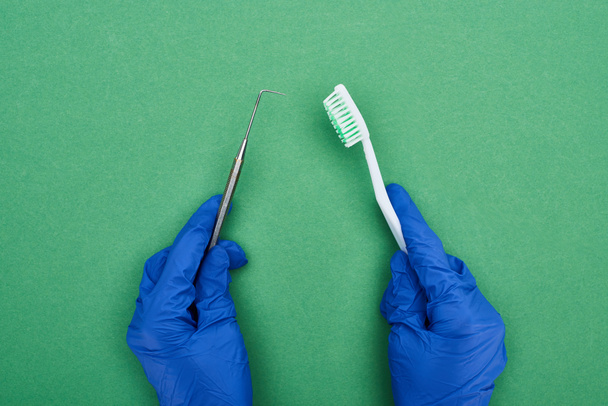 обрізаний вид стоматолога, який тримає стоматологічний скребок і зубну щітку на зеленому
  - Фото, зображення