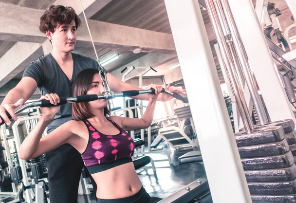 Vrouw is trainen in fitnessapparaat met mannelijke trainer is hel - Foto, afbeelding