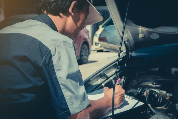 Professionelle Kfz-Reparaturtechniker überprüfen den Motor anhand der Checklisten-Dokumente, um sicherzustellen, dass sie gemäß den Standards des Service-Centers überprüft werden.. - Foto, Bild