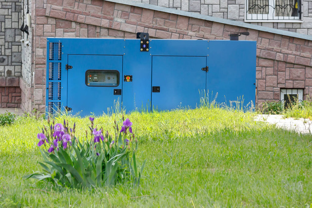 Een bloembed van irissen op de achtergrond van een diesel generator voor noodstroomvoorziening tegen de wand van het medisch centrum bij goed weer. - Foto, afbeelding