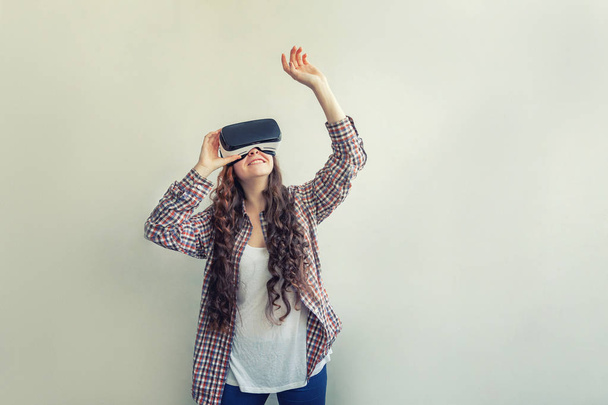Sonríe mujer joven usando realidad virtual gafas VR casco auriculares sobre fondo blanco. Smartphone con gafas de realidad virtual
 - Foto, Imagen
