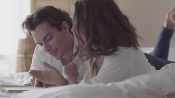 Happy young couple lying on the bed reading the book close-up. Beautiful woman and man spending time in bed at home. Concept of happiness and tenderness, people in love. - Footage, Video