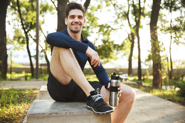 Portrait of beautiful athletic man sitting on bench and holding  - Foto, immagini