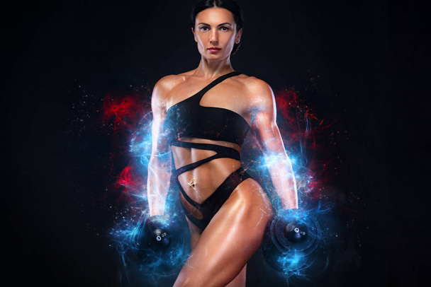 Strong muscular bodybuilder athletic woman pumping up muscles with dumbbells on black background. Workout bodybuilding and energy concept. - Φωτογραφία, εικόνα
