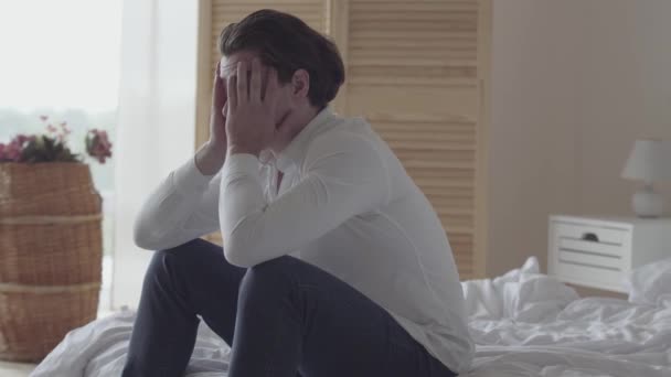 Depressed young man alone at home or hotel room. The guy falling on his bed, he is sad, tired and exhausted. Mental injury, disorder, bad mood. Side view - Video, Çekim