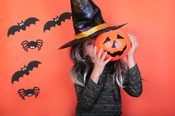 lachen kind meisje met pompoenen in heks kostuum op Halloween Party. Halloween viering concept, oranje enge achtergrond met spinnen en vleermuizen - Foto, afbeelding
