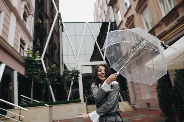 Portrait of a cheerful woman posing with umbrella near the cafe. - Fotó, kép