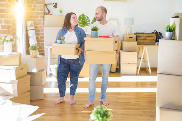Young couple moving to a new home, smiling happy holding cardboard boxes - Foto, Imagem