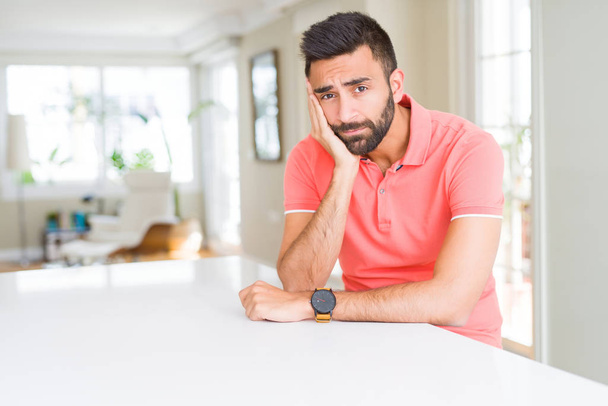 ハンサムなヒスパニック系の男性は自宅でカジュアルな t シャツを着て疲れを見て、交差した腕のうつ病の問題に飽きています. - 写真・画像
