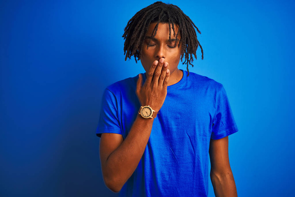 Afro american man with dreadlocks wearing t-shirt standing over isolated blue background bored yawning tired covering mouth with hand. Restless and sleepiness. - Photo, Image