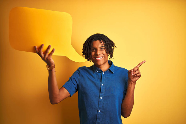 Afro american man with dreadlocks holding speech bubble over isolated yellow background very happy pointing with hand and finger to the side - Фото, зображення
