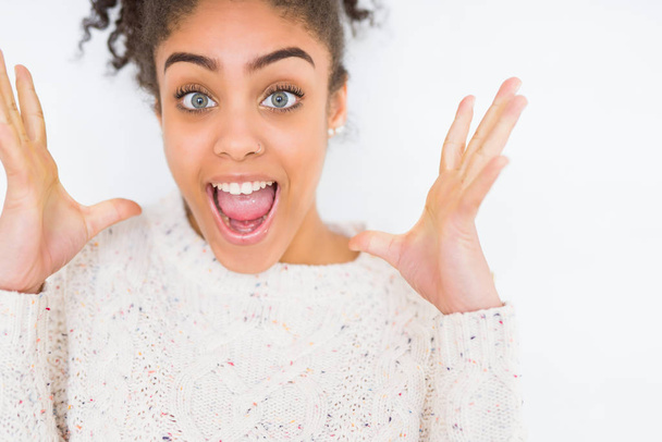 Krásná mladá africká americká žena s afro vlasy nosí ležérní svetr slaví šílený a ohromen pro úspěch s pažemi, vystouplý a otevřené oči křik nadšeni. Vítěz koncept - Fotografie, Obrázek