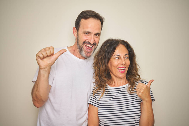 Beautiful middle age couple together standing over isolated white background smiling with happy face looking and pointing to the side with thumb up. - Photo, Image