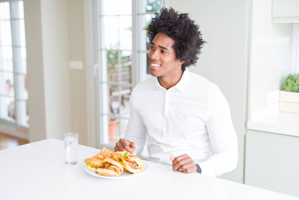 Uomo afroamericano affamato mangiare hamburger per pranzo guardando da un'altra parte con il sorriso sul viso, espressione naturale. Ridere fiduciosi
. - Foto, immagini