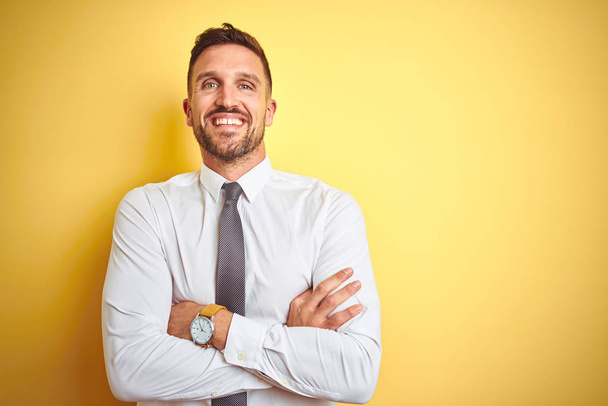 Νέος όμορφος επιχειρηματικός άνθρωπος φορώντας κομψό λευκό πουκάμισο πάνω από κίτρινο απομονωμένο φόντο χαρούμενο πρόσωπο χαμογελώντας με σταυρωτά χέρια κοιτάζοντας την κάμερα. Θετικός άνθρωπος. - Φωτογραφία, εικόνα