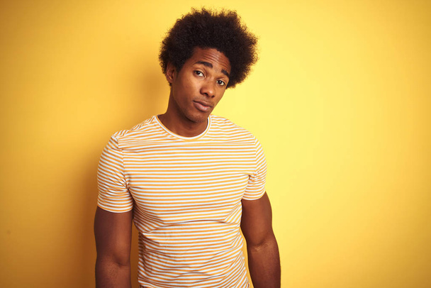 American man with afro hair wearing striped t-shirt standing over isolated yellow background looking sleepy and tired, exhausted for fatigue and hangover, lazy eyes in the morning. - Фото, зображення