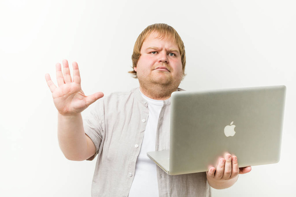 Caucasian plus size man holding a laptop standing with outstretched hand showing stop sign, preventing you. - Photo, Image