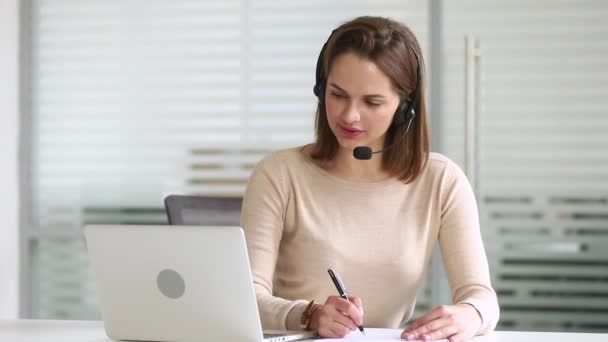 Business vrouw receptioniste dragen headset kijken naar laptop maken notities - Video