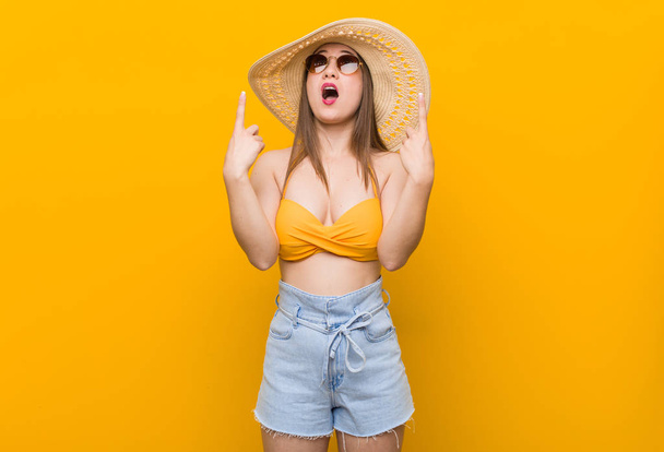 Mujer joven caucásica con un sombrero de paja, mirada de verano apuntando al revés con la boca abierta
. - Foto, imagen