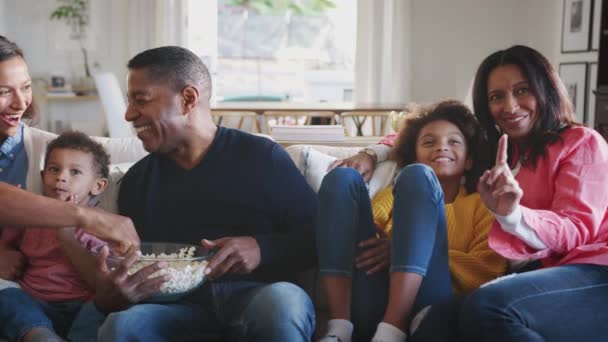 Three generation African American family sitting on the sofa watching TV and eating popcorn, panning shot - Footage, Video