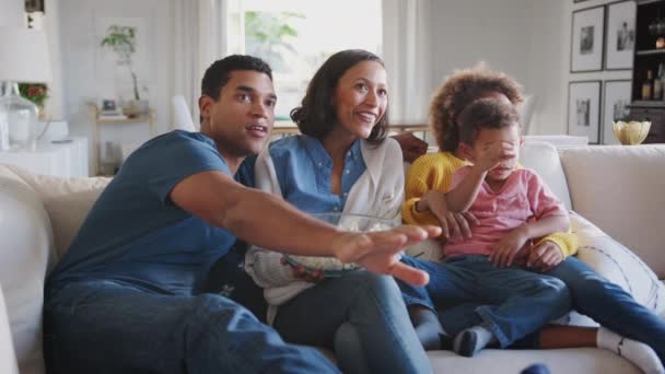 Young African American family sitting on the sofa at home watching TV and eating popcorn - Imágenes, Vídeo