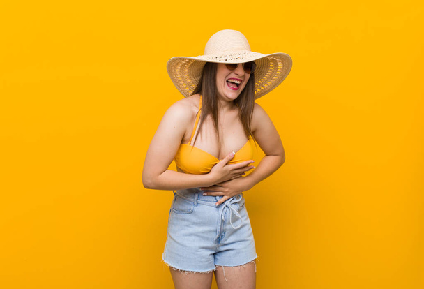 Mujer caucásica joven con un sombrero de paja, mirada de verano ríe felizmente y se divierte manteniendo las manos en el estómago
. - Foto, imagen