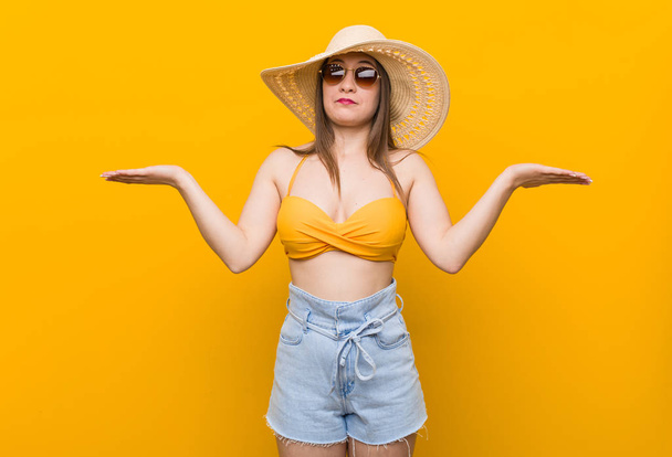 Mujer caucásica joven con un sombrero de paja, mirada de verano dudando y hombros encogiéndose de hombros en gesto de interrogación
. - Foto, imagen