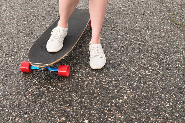 Close-up of female legs in rag sneakers on a longboard on the background of asphalt at sunset. Big skateboard with girl legs. Youth leisure concept - Fotó, kép