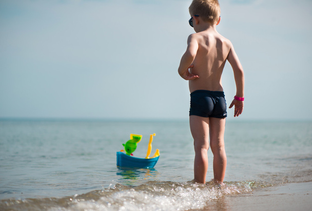 Little boy in sunglasses playing with toy boat - Foto, imagen