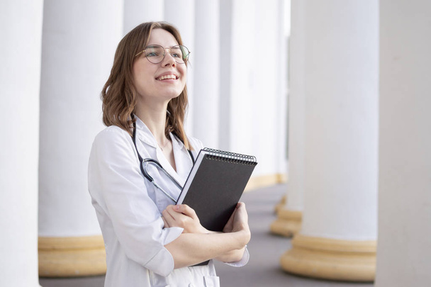 young girl student at a medical university standing in the corridor, portrait of an attractive nurse near the hospital, happy female doctor with a stethoscope in uniform - Foto, imagen