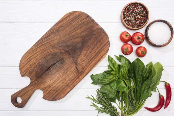 top view of cutting board, cherry tomatoes, greenery, chili peppers, salt and spices  - Photo, Image
