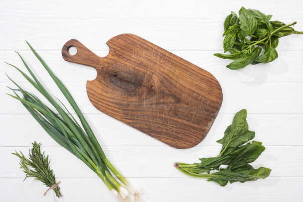 top view of wooden cutting board and greenery on white table  - Foto, Bild
