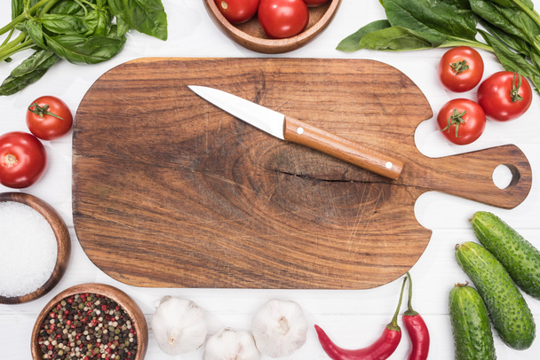 top view of cutting board, cherry tomatoes, greenery, chili peppers, salt, garlics, knife and spices  - 写真・画像