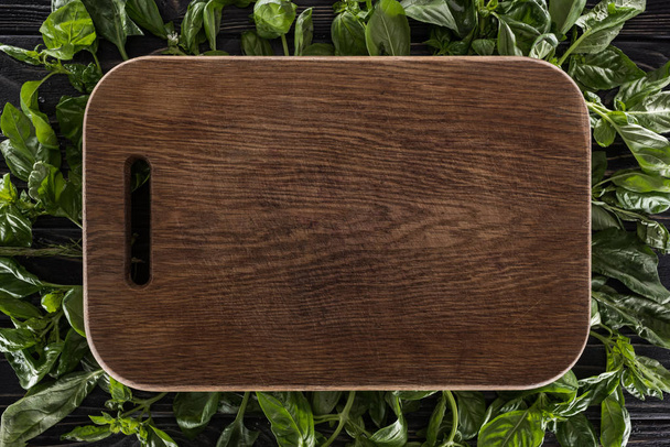 top view of wooden cutting board on leaves of basil  - 写真・画像