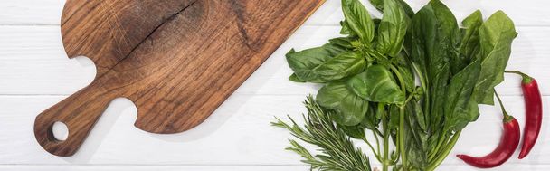 panoramic shot of wooden chopping board, chili peppers and greenery - Fotografie, Obrázek