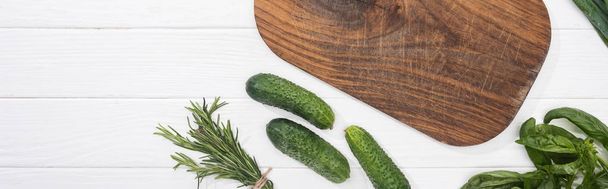 panoramische foto van houten snijplank, komkommers en groen - Foto, afbeelding