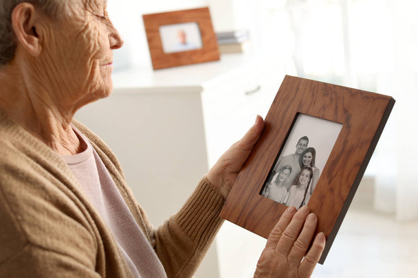 Elderly woman with framed family portrait at home - Фото, изображение