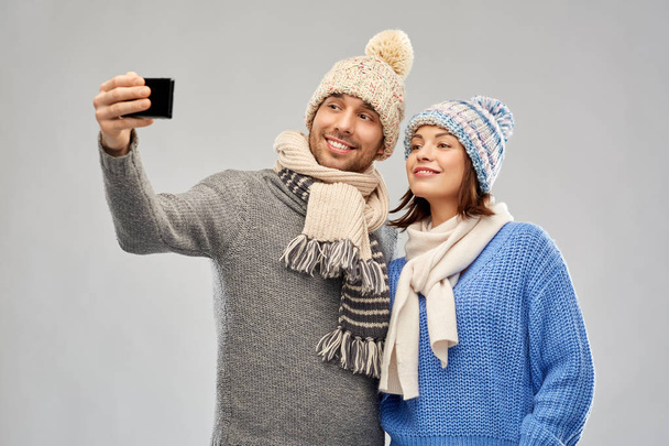 couple in winter hats taking selfie by smartphone - Фото, изображение