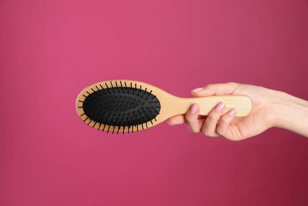 Woman holding wooden hair brush against crimson background, closeup - Foto, afbeelding