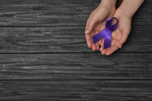 Woman holding purple awareness ribbon on black wooden background, top view with space for text - Foto, immagini